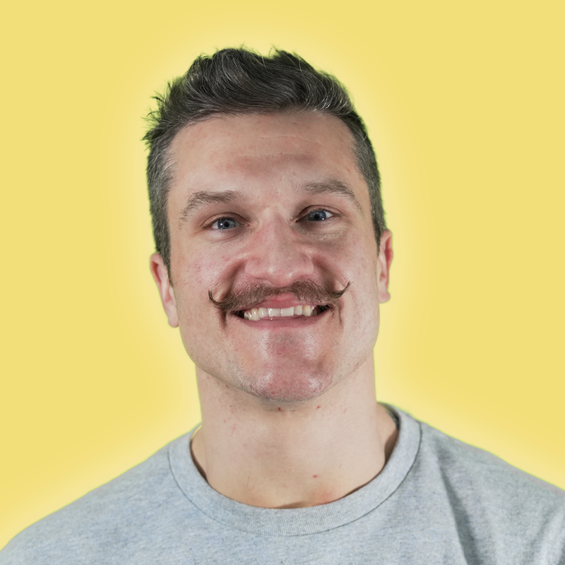 Monroe Miller smiling warmly against a bright yellow background, wearing a gray shirt