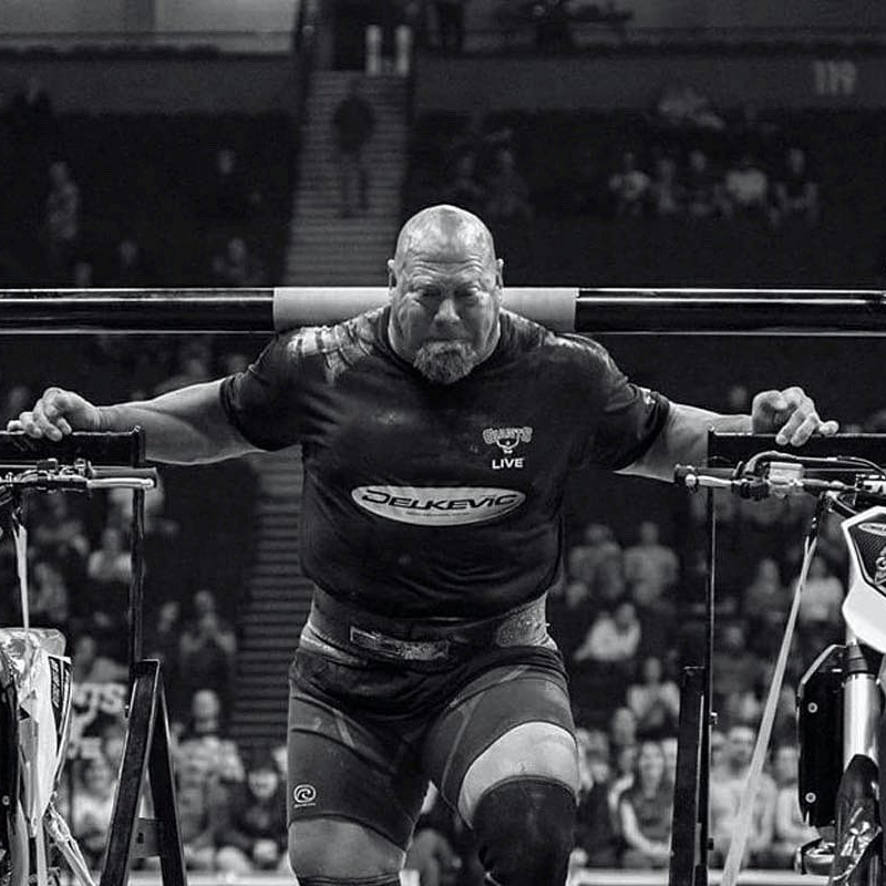 Nick Best competing in a strongman event, carrying heavy weight with intense focus