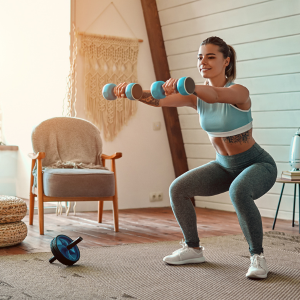 Woman completing home workout in squat position holding weights with her arms straight out