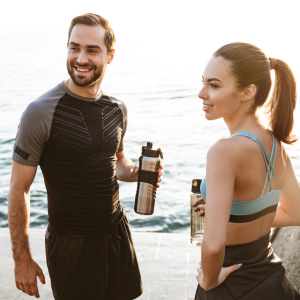 Man and women holding water bottles on a beach looking into the distance